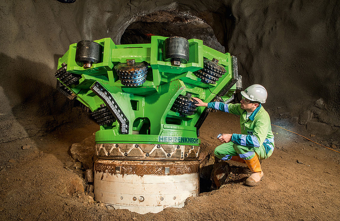 进入竖井前钻井装置上的绿色铰刀和旁边一名工地工人的照片
